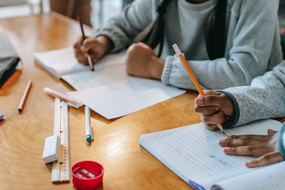 Close-up shot of young students writing on a notebook in classroom