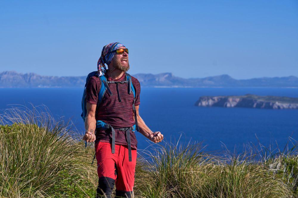 Male traveler standing on cliff and celebrating achievement
