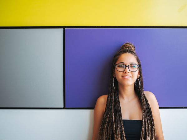 Charming teenage girl with braids in sunglasses nearby colorful wall