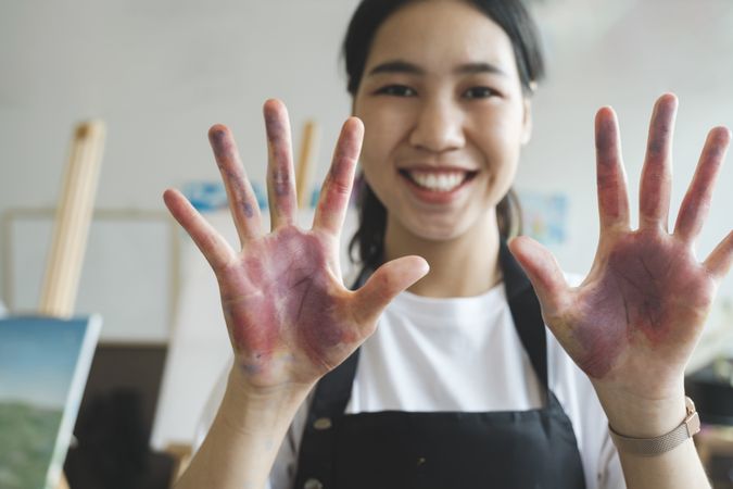 The artist creates a frame with her hands soiled with watercolor paints.