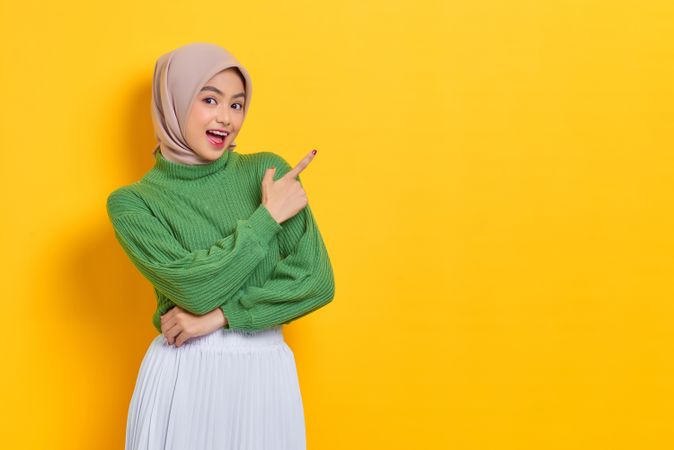 Excited woman in headscarf pointing her finger towards the side