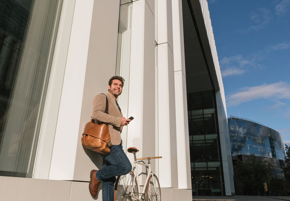 Businessman with smartphone leaning on building on city street