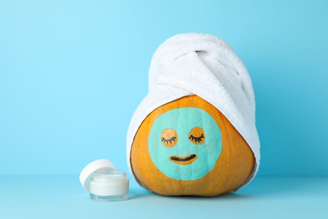 Cream, pumpkin with facial mask and towel on blue background, copy space