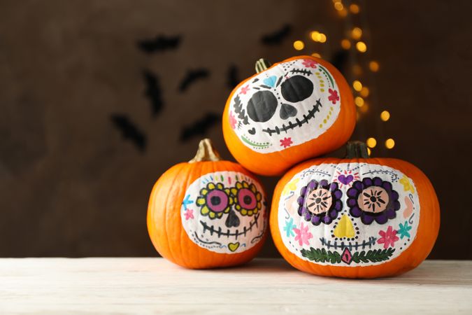 Pumpkins with catrina skull makeup on brown background with blurred lights