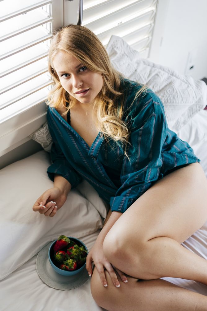 Young woman lying on bed with strawberry bowl