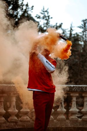 Man in red shirt and pants flashing with red smoke gun standing in the woods