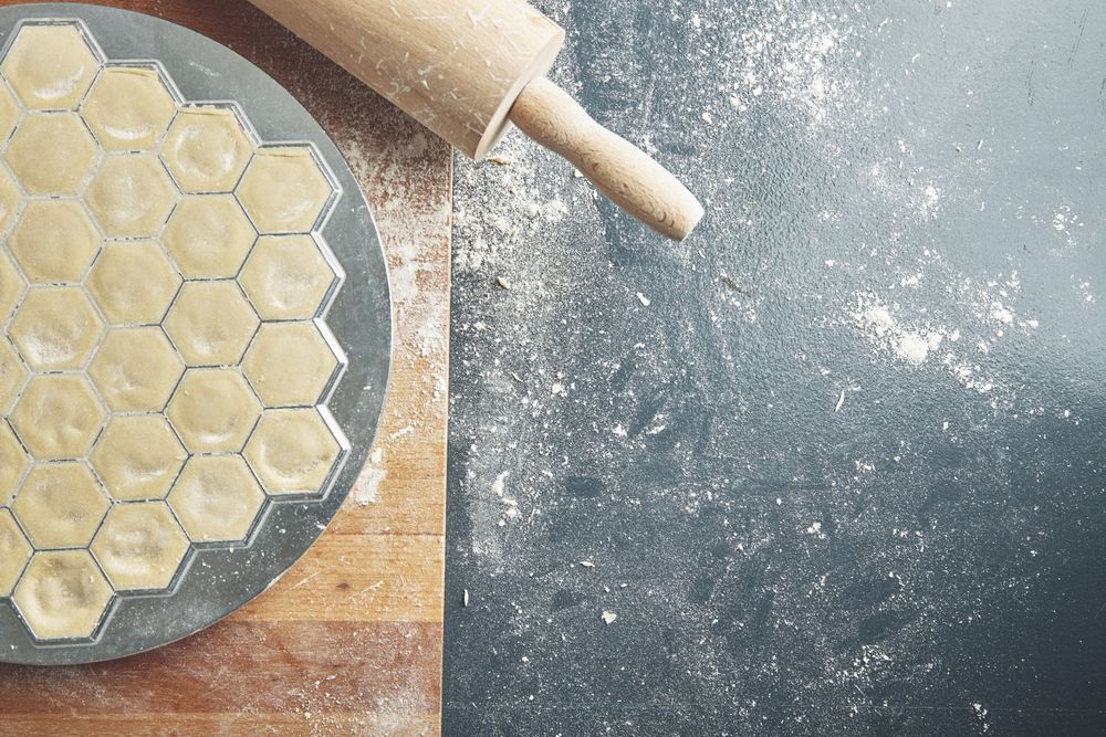 Top view isolated on left ready ravioli in mold, rolling pin near on old blue table