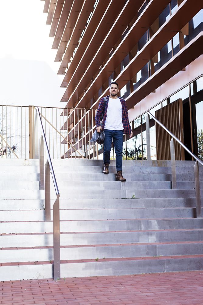 Smiling man in plaid shirt walking down stairs on a sunny day, vertical