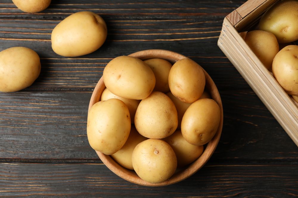 Top view of bowl of potatoes next to basket of potatoes on dark table