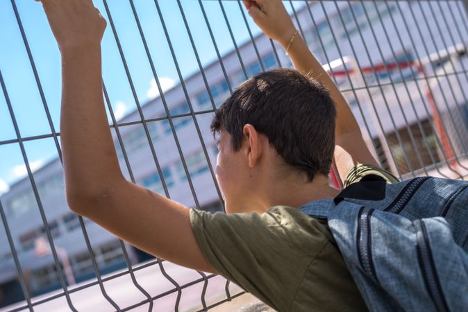 Boy holding gate with both hands looking into school yard