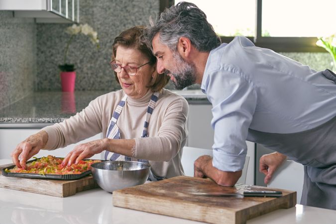 Unshaven man with aged mother cooking pizza together