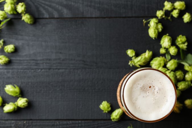 Glass of beer and hop cones on wooden background, top view