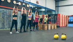 Sportswomen with kettlebells and sportsmen in background