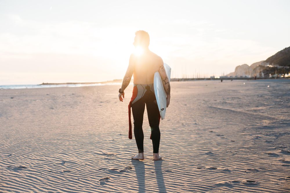 Man walking with surfboard at sunset