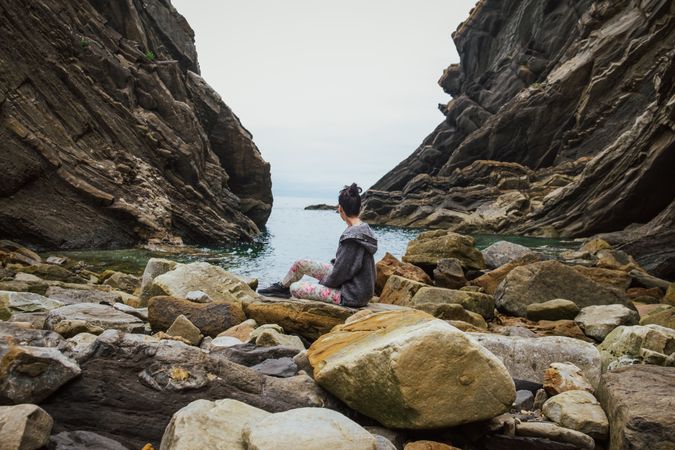 Woman on boulders shore against gorge and seascape in overcast weather