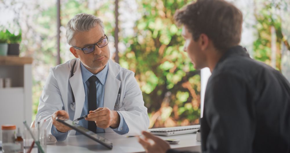Adult General Practitioner Showing Recovery Treatment Results on Tablet Computer to a Young Male Patient