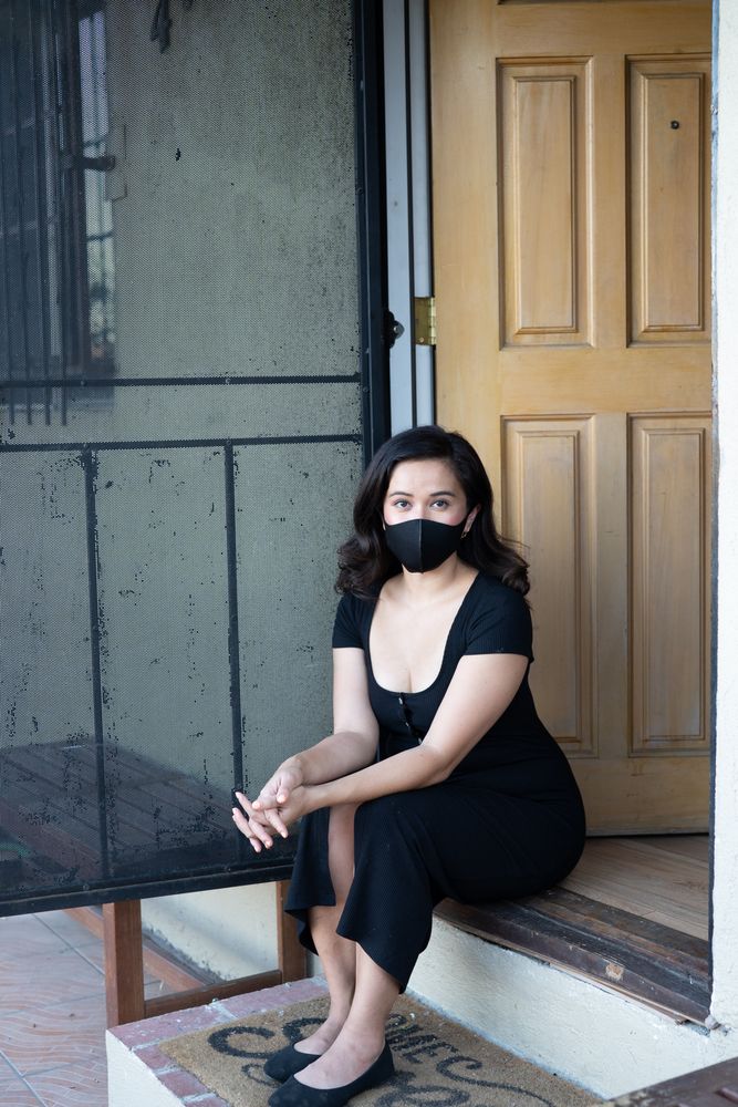 Woman in PPE mask sitting on front porch looking at camera