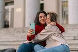 two students smiling taking a selfie sitting on the stairs of the college.