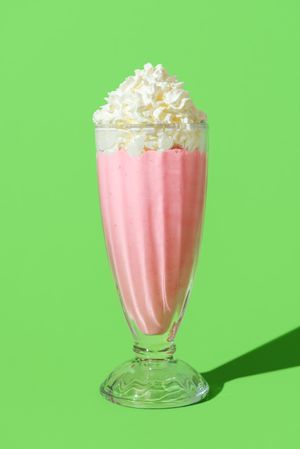 Strawberries milkshake glass in bright light, isolated on a green background