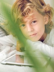 Charming preteen boy lying with tablet and looking at camera