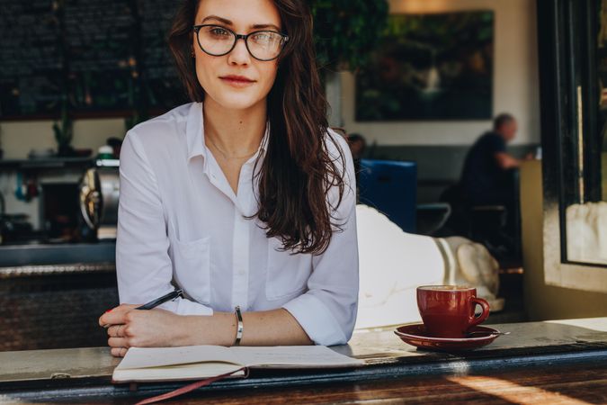 Woman in eyeglasses relaxing in cafe with notebook and coffee