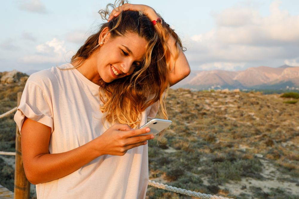 Young hipster browsing smartphone and smiling while walking in nature