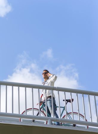 Looking up at male on bike on bridge using phone