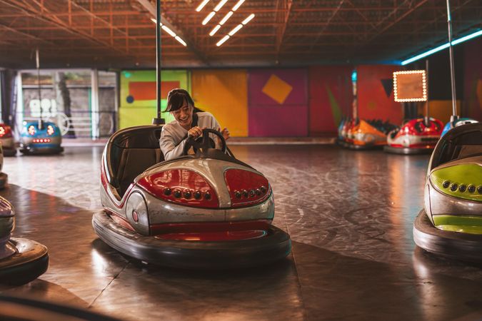 Happy young woman driving a bumper car at amusement park