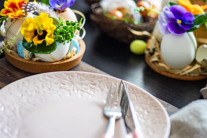 Easter holiday table setting with close up of decorative eggs with colorful flowers around a pink plate
