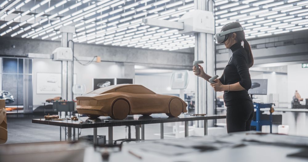 Female Car Designer Wearing a Virtual Reality Headset and Using Controllers to Work on a Concept Car Made Out of Plasticine Modeling Clay.