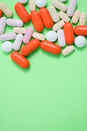 Top view of variety of colorful pills and vitamins on green table with copy space