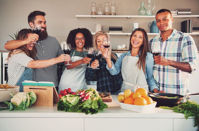 Multi-ethnic friends toasting with red wine in the kitchen together