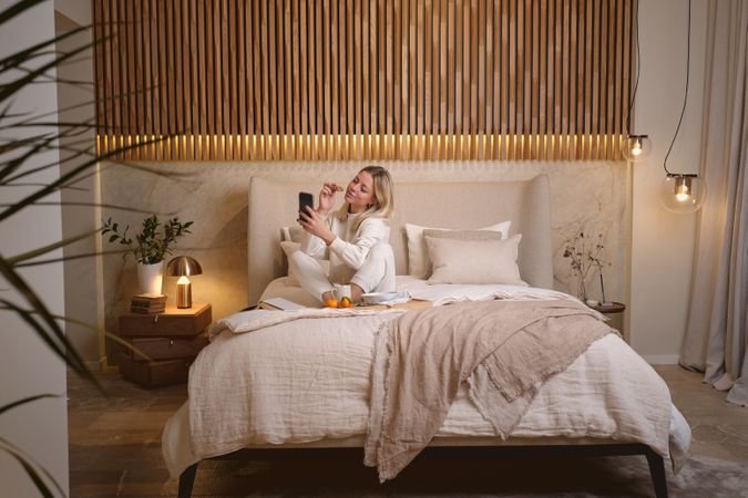 Woman with cookie taking selfie in bed