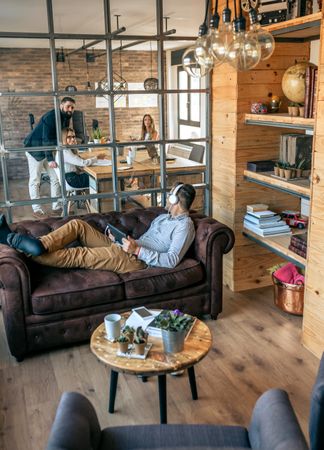 Businessman lying on an office sofa talking to his coworkers