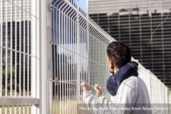 Man leaning on a metallic fence while looking up to the business buildings 4d8ada
