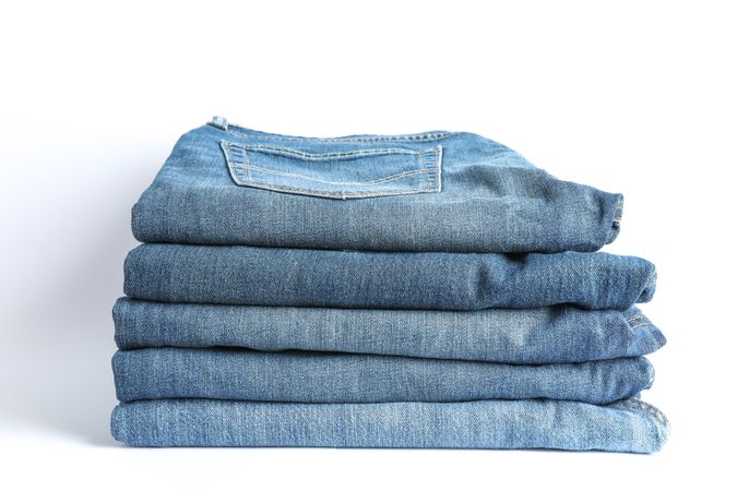 Stack of blue jeans on light background, space for text