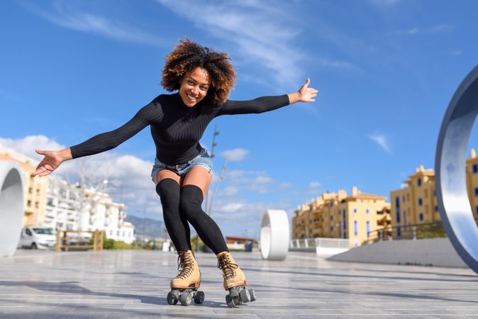 Happy woman with afro and arms spread roller skating outside