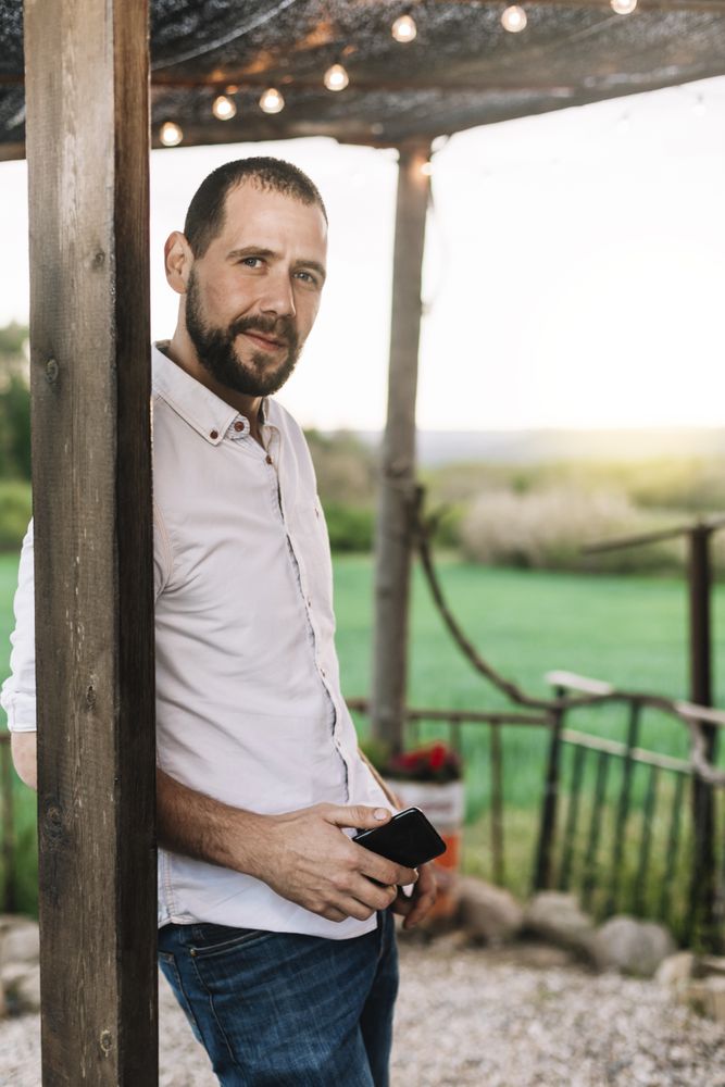 Bearded man standing outside home while using a mobile phone