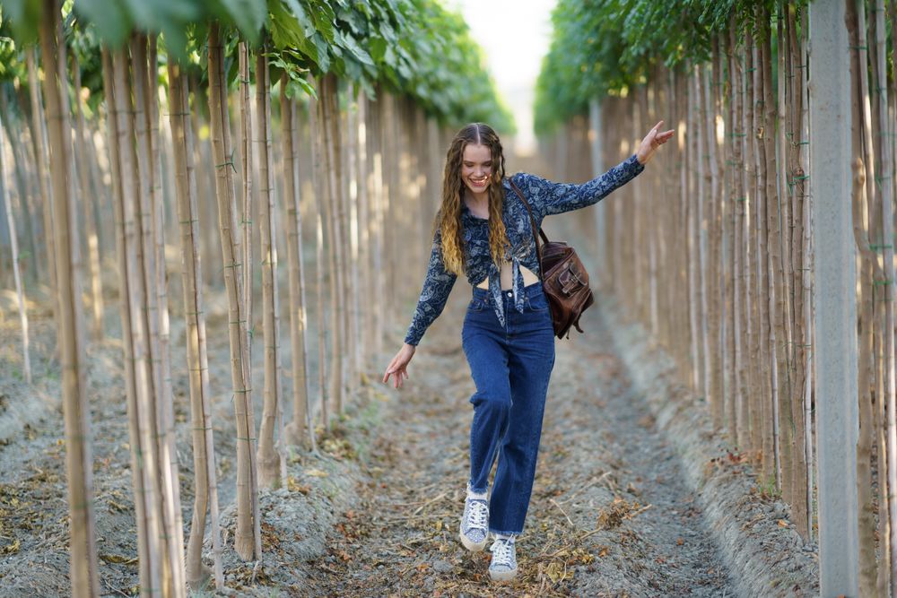 A Joyful Young Woman Walking Through Lush Green Rows of Beautiful Trees in Nature