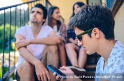 Young man looking a smartphone outdoors with his friends in background 4d88WD