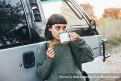 Woman leaning on camper van sipping coffee 0gPy75