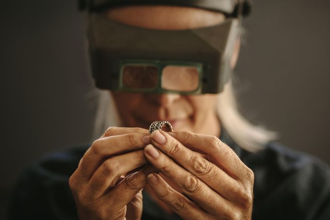 Woman goldsmith examining sliver designer ring using magnifying glass