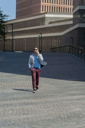 Man with sunglasses walking with hand on pocket outside in the sun