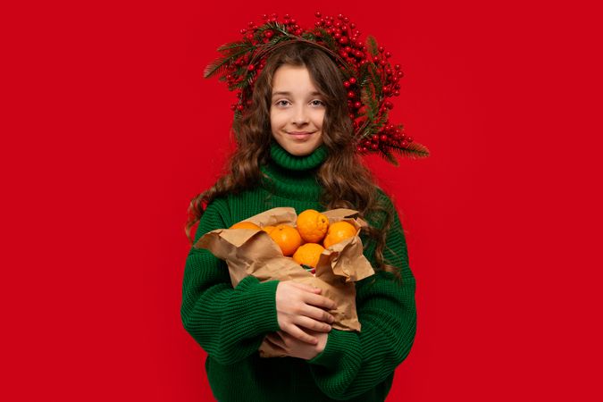 Young girl in green sweater holding paper bag of oranges