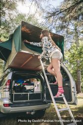 Woman standing in ladder closing tent above car bGRo8v