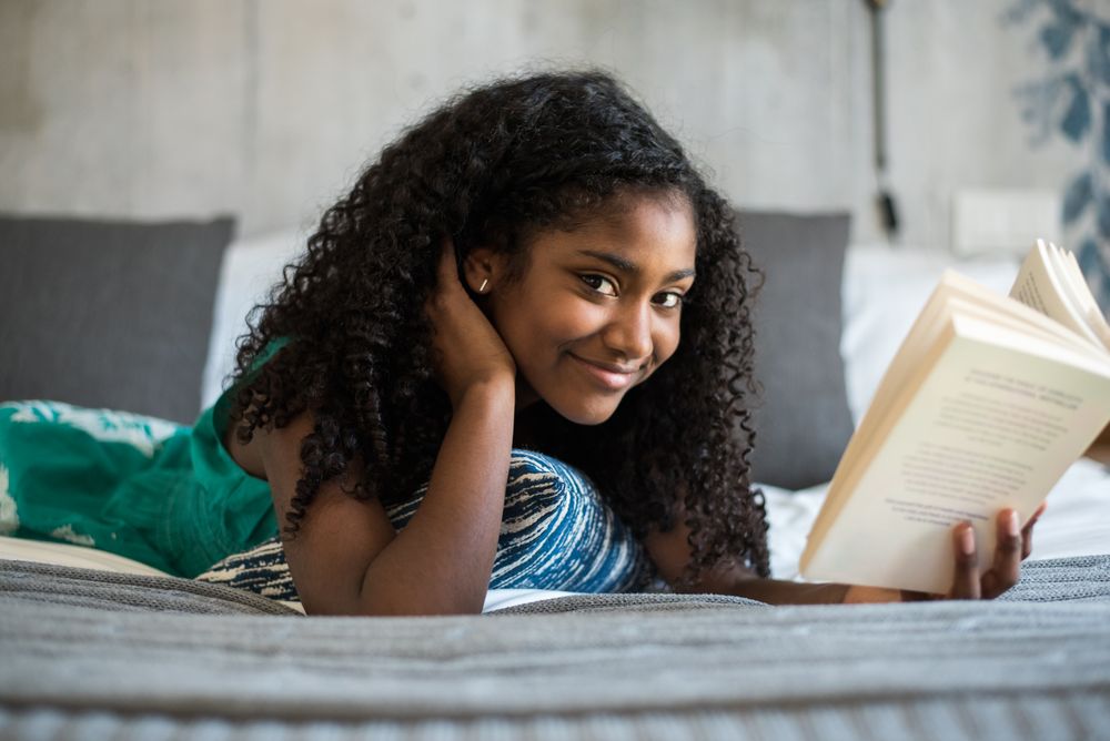 Black teenage reading a book on bed