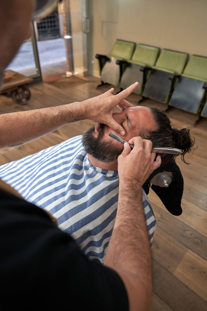 Unrecognizable barber trimming beard of client