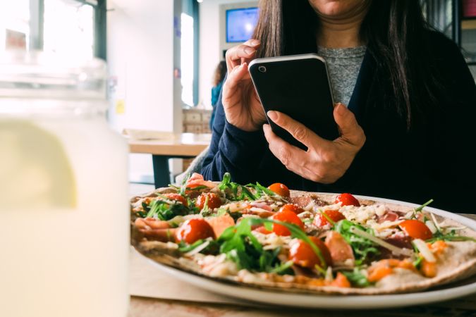 Woman with smartphone near fresh salad on table