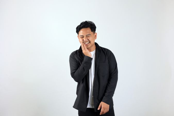 Young Asian Man Standing, Touching Mouth with His Hand