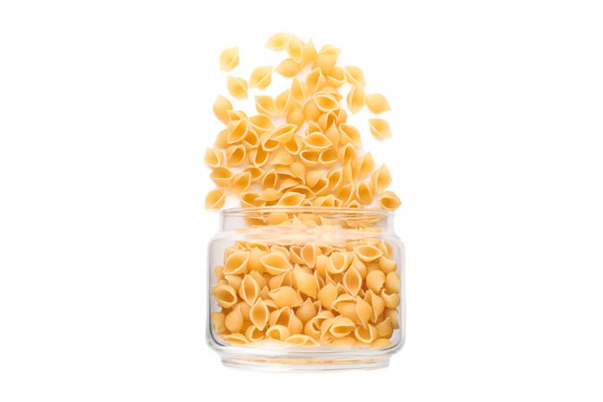 Pasta in glass jar isolated on light background. Uncooked whole wheat pasta